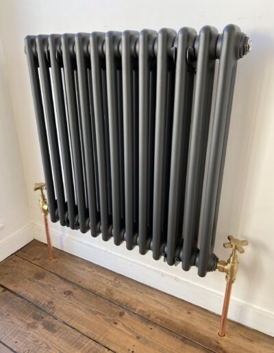 Anthracite column radiator on stripped wood floor with traditional brass valves