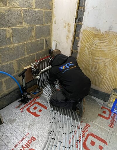 AZ Plumbing engineer installing an underfloor heating manifold over insulation board, North London